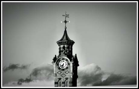 A dramatic black and white photo of the top half of the tower, with rolling dark clouds behind it