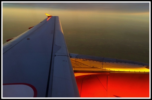 A photo looking out of the window onf the plane overlooking the wing and engine, with a beautiful coloured sunrise panarama!