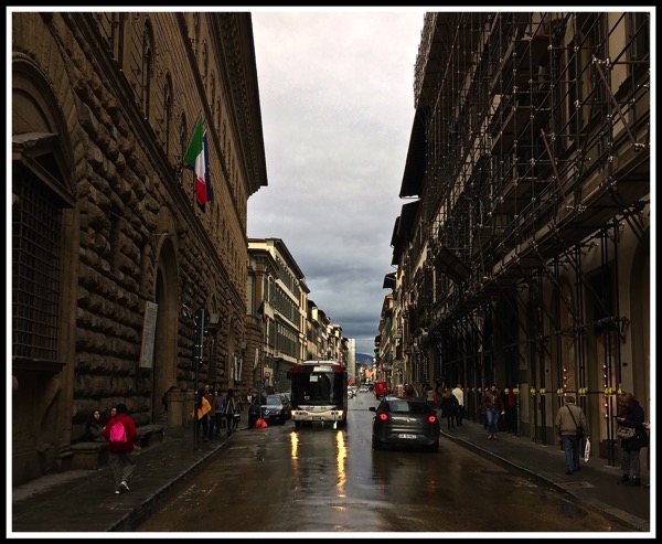 stood in the centre of the road with the palazzo medici riccardi on the left and a bus with its streaming light reflecting in the wet road